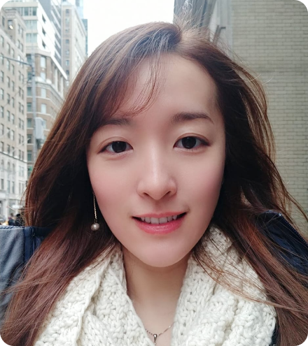 profile picture of ginni lam smiling with long reddish hair and a white scarf and circle earrings on a sunny day against the new york city background