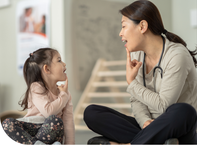 Asian adult woman doing speech therapy with a 5-year-old girl inside a home