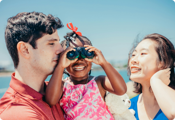 white dad holding a black daughter with asian mom on the beach