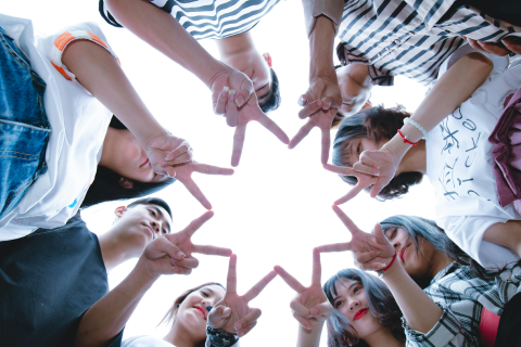 bottom view of several young adult friends using their hands to make a V shape in a circle to form a star